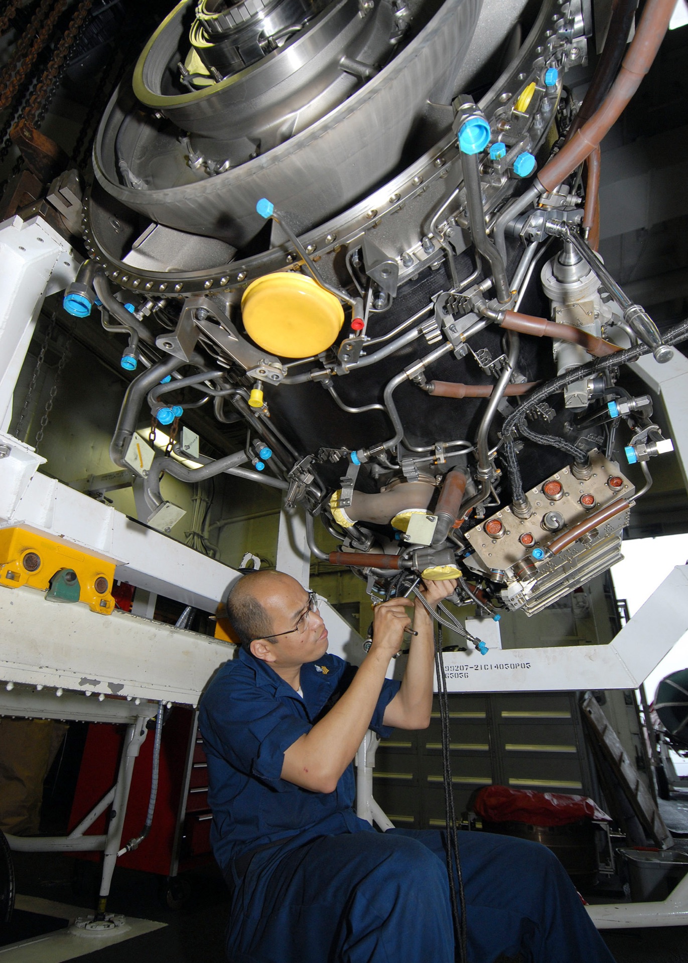 Aircraft technician inspecting wiring and mechanical assemblies below an aircraft