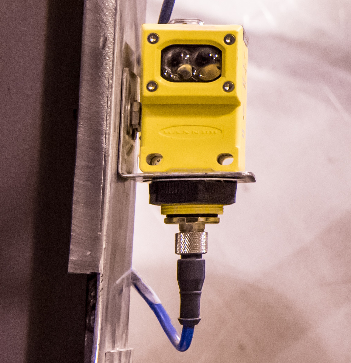 Yellow photoelectric sensor mounted on industrial equipment with a cable connection below