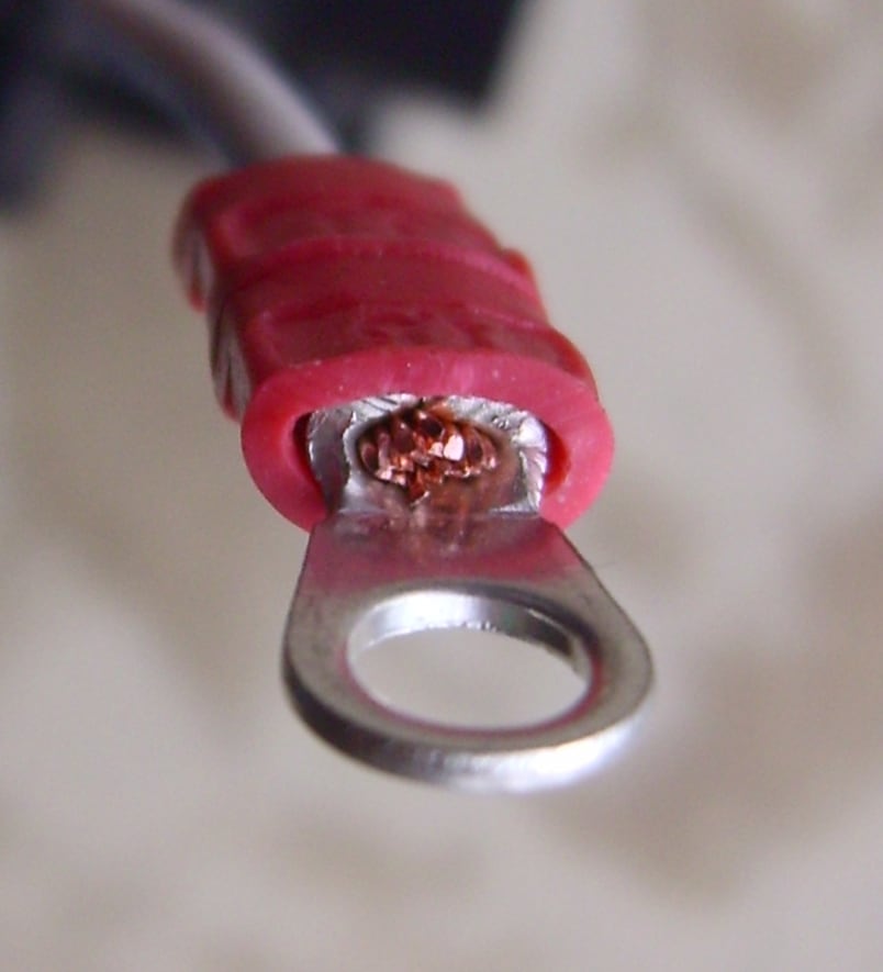 A small crimped ring terminal illustrates barrel and palm geometry; high-voltage lugs need their own approved specification.