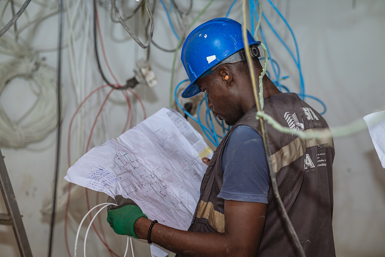 Electrician reading a paper electrical schematic beside installed wiring