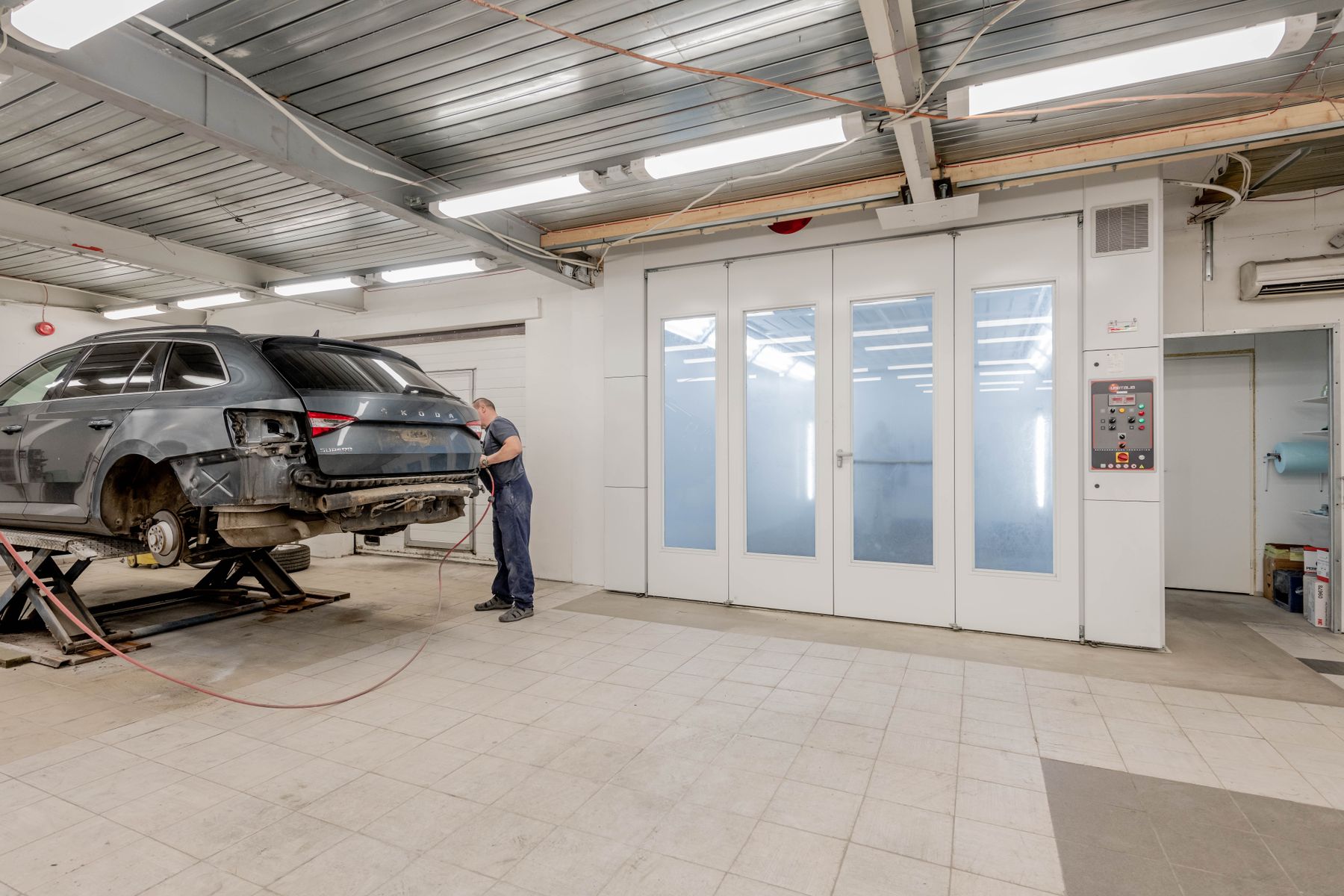 Technician beside a lifted vehicle in a body-repair workshop
